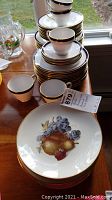 Stacked dinnerware and fruit-themed plates featuring grapes and pears with gold trim, showing spode and baronet china items