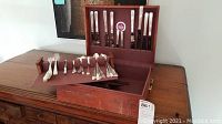 Wooden chest open showing knives in lid slots and assorted flatware pieces in base