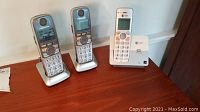 Three cordless telephones on a table: one AT&T white model with base, two Panasonic silver models with bases.