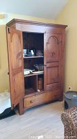 Front view of vintage pine wood armoire with doors open showing shelves and drawer