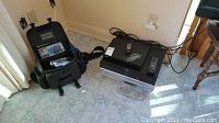 Black soft carrying case with Sony camcorder next to stack of three players and remotes