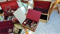 Open vintage jewelry boxes showing assorted costume jewelry items like necklaces, earrings, and brooches inside.