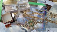 Several gold-tone chains and necklaces laid out with a decorative brooch and some small items in boxes on a reflective surface.