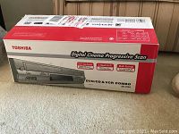 Toshiba DVD/CD and VCR combo in its original box showing front panel and key features including Digital Cinema Progressive Scan, DVD/CD and VCR combo, multi-format playback.