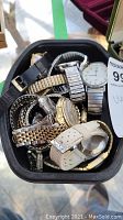 Overview of mixed lot of men's and ladies' watches with various metal and leather bands inside a black container.