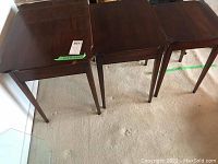 Front view of three dark brown wooden nesting tables lined up from largest to smallest on carpeted floor.