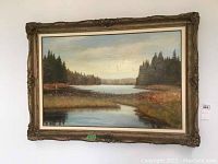 Framed oil painting on board featuring a river or lake surrounded by evergreen trees and a cloudy sky.