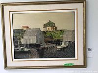 Framed painting showing wooden fishing shacks and boats at Peggy's Cove with a green-roofed house on the hill.