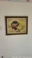 Front view of original oil painting showing framed still life scene with a pottery jar, brass teapot, eggs, and stone.