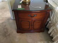 Front view of one wooden Drexel nightstand showing drawer with decorative metal handles, two cabinet doors, and glass top.