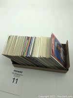 Box containing a large stack of baseball cards viewed from the side showing many cards of varied thickness and some color edges.