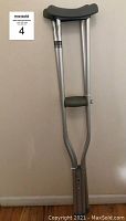 Full view of one aluminum crutch, showing padded underarm and hand grip areas, standing against a white wall.
