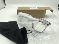 Photo of the clear lens anti fog safety glasses, partially wrapped in protective white tissue, alongside the cardboard box and black drawstring pouch.