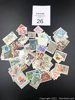 Photo showing about 40 assorted used postage stamps with various images including flowers, architecture, and portraits on a black background.