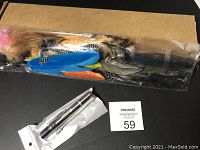 Photo of colorful feather cat teaser toy and silver LED light pen in original packaging, positioned on a black surface with a cardboard box in the background.