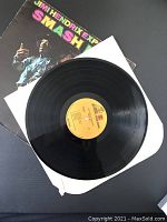 Vinyl record partially out of white sleeve with album cover underneath, showing yellow label on record.