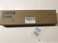 Image of unopened cardboard box with the label 'Laptop Stand' and a simple line drawing of the stand design.