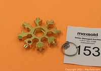 Gold-tone snowflake-shaped multi-tool with multiple wrench and screwdriver cutouts alongside a metal keyring.