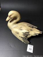 Front angled view of a beige wooden duck figurine showing rounded neck, head, and distressed wings.