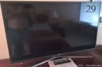 Samsung 40-inch TV on table stand showing the entire front with remote control visible on table.