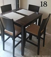 Square dark wood high dining table set with four high back chairs with beige felt seats from angled side view.