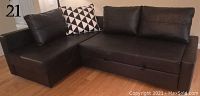 Black leather L-shape sectional sofa with two black and white patterned pillows, shown from front angle.