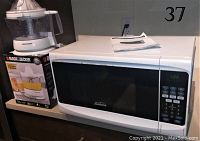 Sunbeam microwave oven on countertop with Black & Decker juicer and box visible to the left.