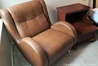 Brown leather reading chair next to a dark brown wood contemporary magazine table, showing chair upholstery, armrest design, and table storage features.