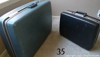 Two hard case suitcases side by side, one blue and larger, the other black and smaller, placed on floor showing exterior condition.