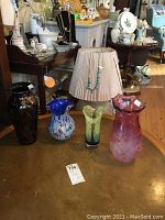 Four art glass vases arranged on a table with a lamp between some of them.