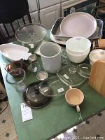 Overall view of baking and kitchen items including pans, mixing bowls, cake stand, and utensils on green table.