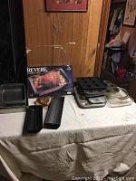 Photo showing assortment of aluminum brownie pans, almond cake pans, copper heart mold, and boxed Revere Ware roasting pan on table.