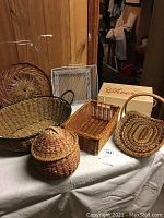 Six baskets of different sizes and materials on a covered table, showing materials (wood, metal, wicker) and shapes.