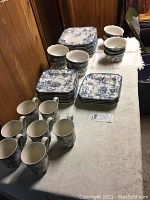 View of china set including stacks of plates, bowls, and mugs on a table.