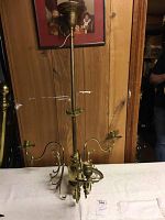 Full view of the three-light brass chandelier standing on a table against a wood panel wall.