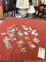 Lot of assorted clip and screw back earrings displayed on a red surface with small plastic bags, various designs and colors visible.