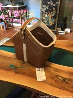 View of the tan faux suede basket tote showing faux fleece lining and handle on wooden table.