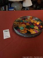 Silver plated round tray with black inset holding many colorful Mardi Gras dabloons in various colors placed on a red surface.
