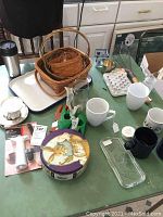 Longaberger basket set nested and placed on enamel tray with mugs and various kitchen items on green table.