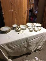 Full view of partial set on white cloth table including various plates, bowls, cups, and a covered serving bowl.