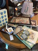 Mixed collection of picture frames and framed art on a wooden table, showing variety of frame sizes and styles.