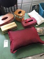 Photo showing two tissue holders, three pillows, and a painted wooden box on a green table surface.