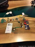 Six pendants and multiple pins displayed on a wooden table with tags and MaxSold label present.