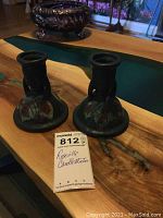 Pair of Roseville candlesticks on wooden table with seller lot tag visible.