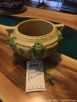 Overall angled view showing bowl shape, handle details, and visible embossed floral and grape decorations in green and brown glaze.