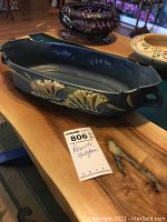 Elongated Roseville pottery bowl with blue glaze and yellow foxglove flower reliefs, placed on wooden table with background items visible but not included.