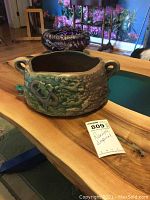 Side view of the Roseville pottery bowl showing textured green and brown glaze, applied decorative motifs, and two small handles.