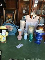View of nine assorted ceramic vases on a green table, including the blue Roseville Gabriella bamboo vase, the yellow figurine vase, and a tall white textured vase