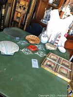 Table display of assorted shell-shaped plates, gold-tone shell bowl, three clear glass fish-shaped dishes, white ceramic lighthouse figurine, and small nautical plates including sailboat and lighthouse themes.