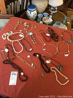 Photo of 16 short necklaces and chokers laid out on a red cloth, featuring various bead, stone, and metal chain styles.